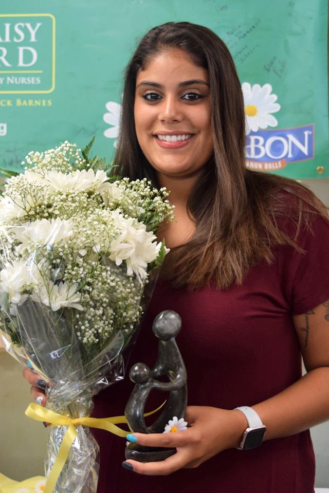 Nancy Parkey smiling and holding a bouquet of white flowers and the Healer's Touch sculpture.